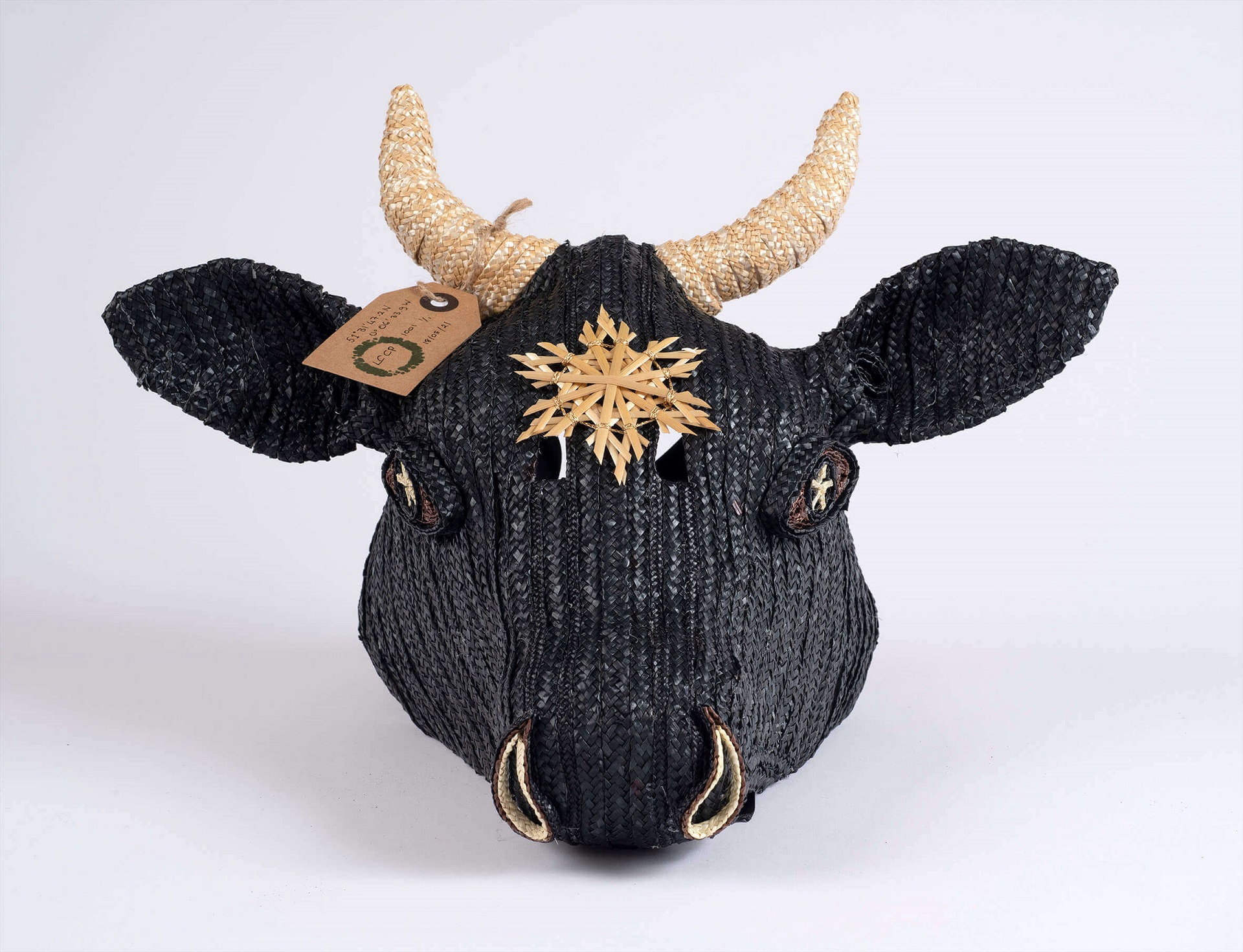 Photograph of a cow's head made from black wicker with a straw star on its forehead