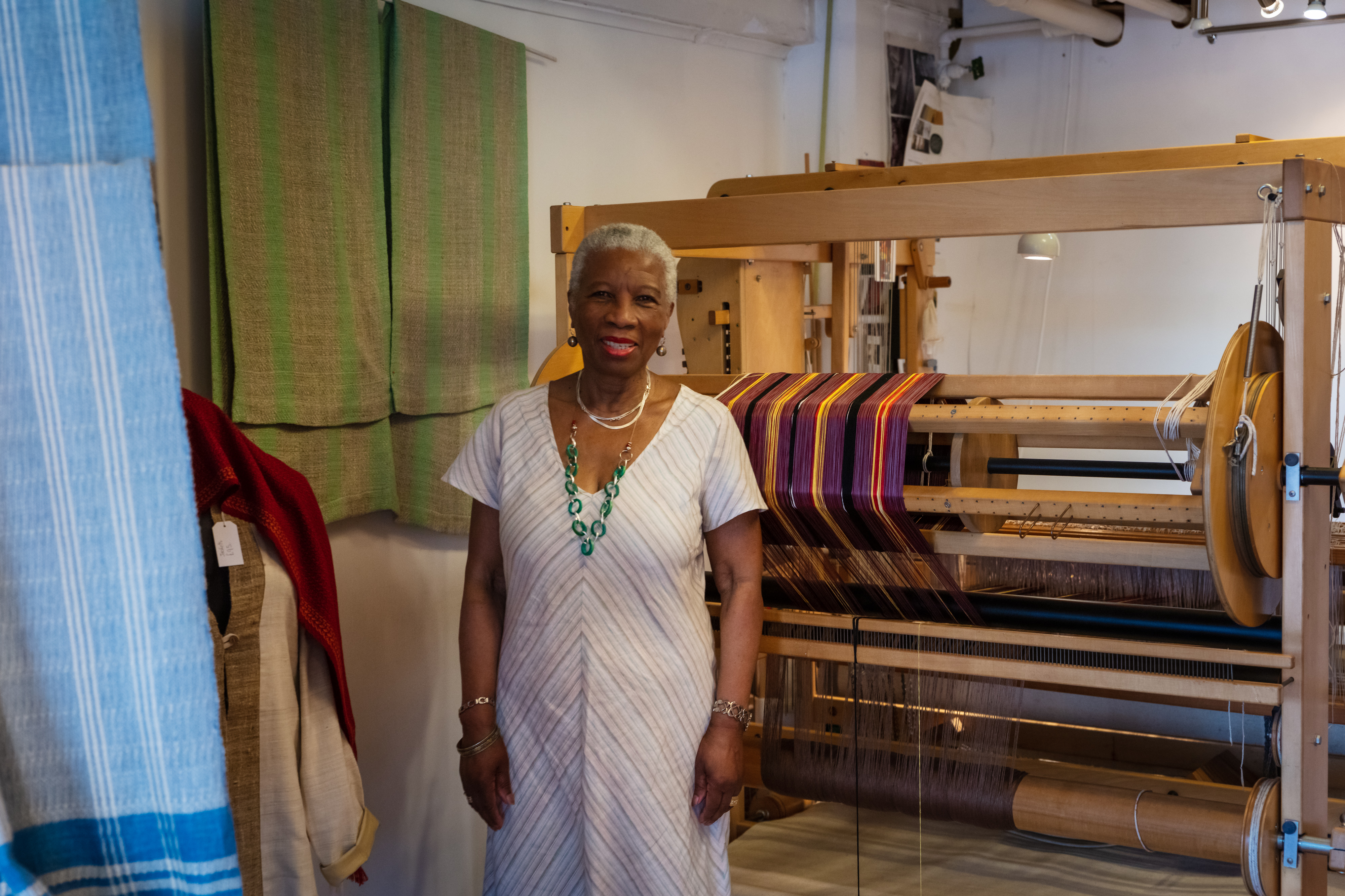 Doreen from Archipelago Textiles stands infront of her loom with handwoven textiles around her in her Oxo Tower Wharf studio