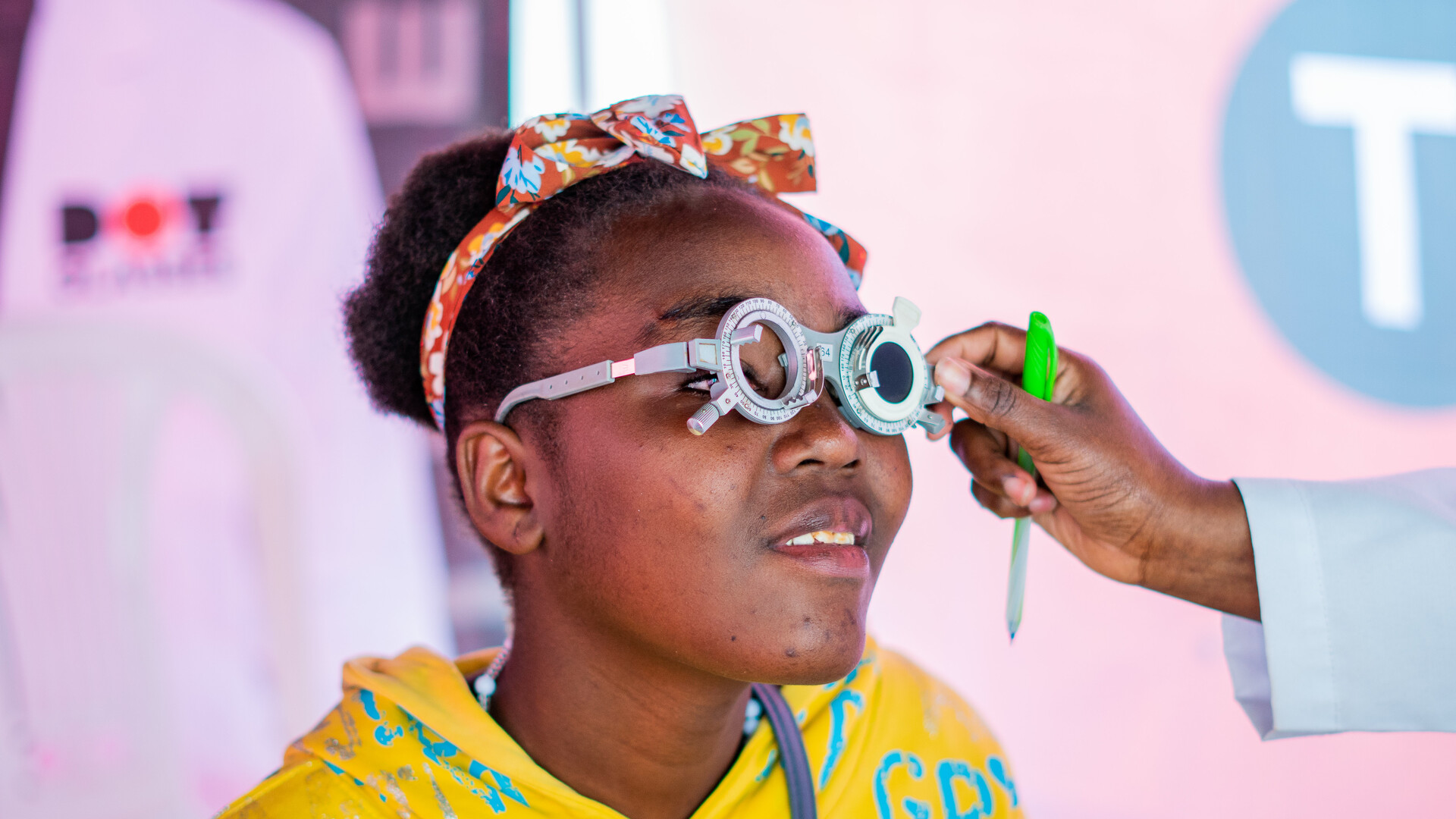 Women in a bright yellow top and red colourful headband, being fitted with glasses within the community