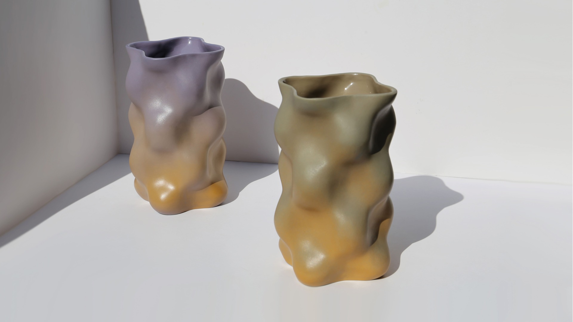 Two sculptural porcelain vases, with soft organic forms and graded glazes in warm desert tones inspired by changing daylight.