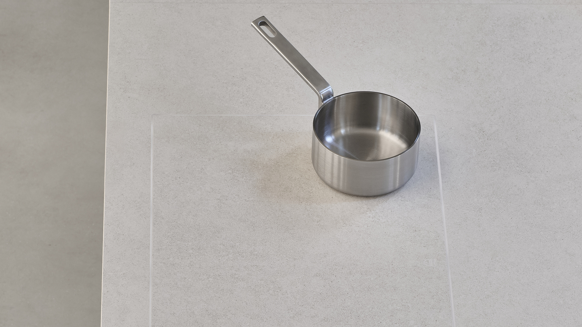 Stainless steel saucepan on a beige countertop, over the outline of a concealed induction cooktop.