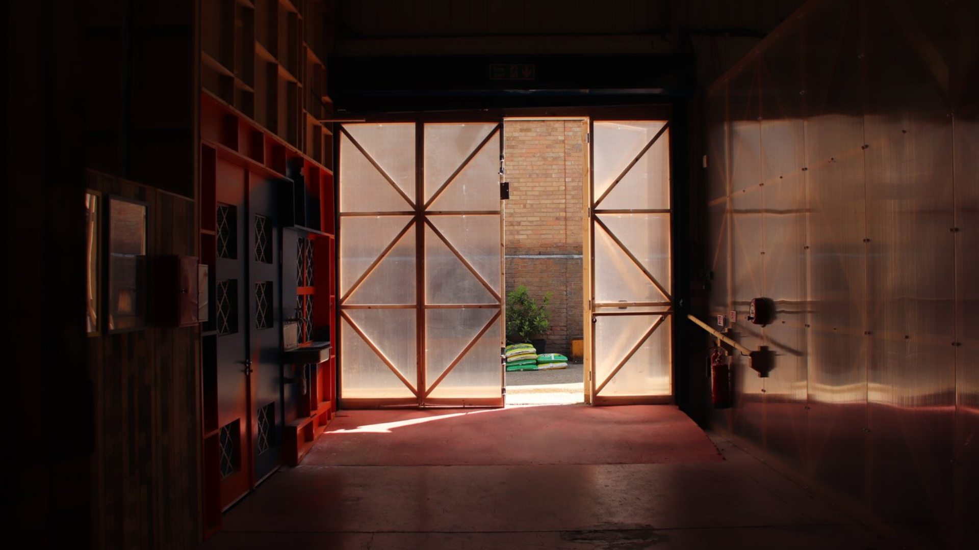 Image shows a large door made of polycarbonate showing an alley way with greenery outside.