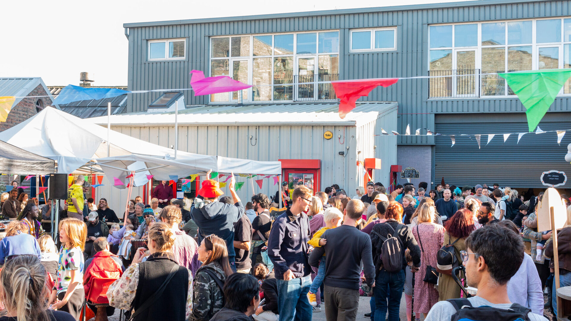 People are gathered in front of a building, there is bunting and gazebos