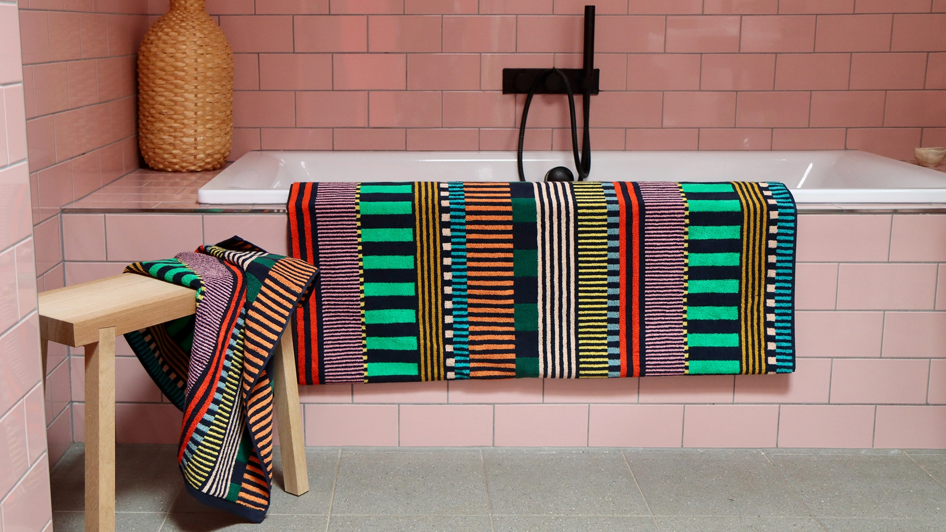 A pink tiled bathroom with multicolour striped towels
