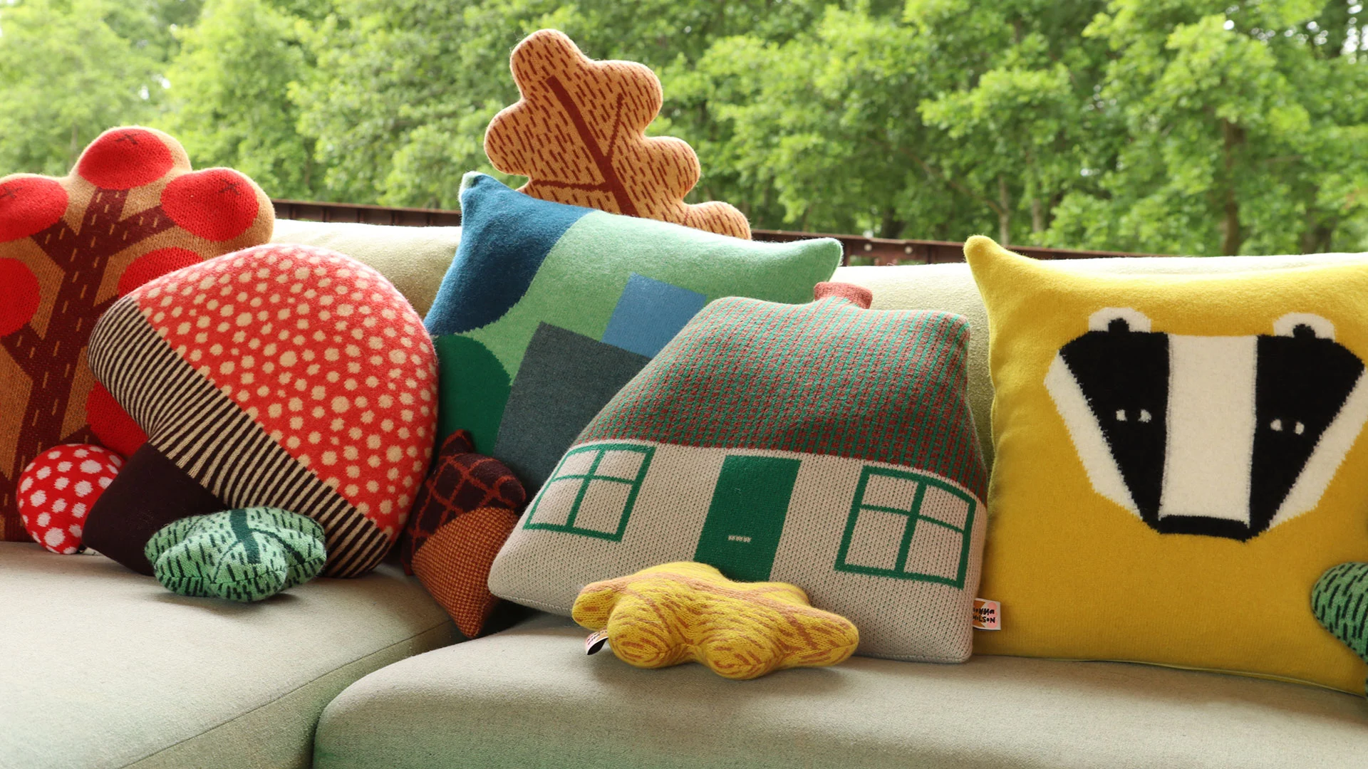 A collection of shaped, knitted woollen cushions on a sofa.