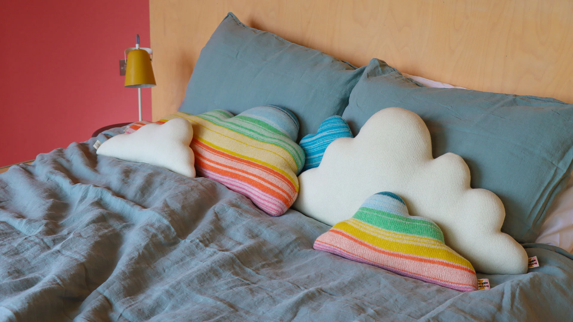A pair of multicolour rainbow striped cloud-shaped cushions on a bed.
