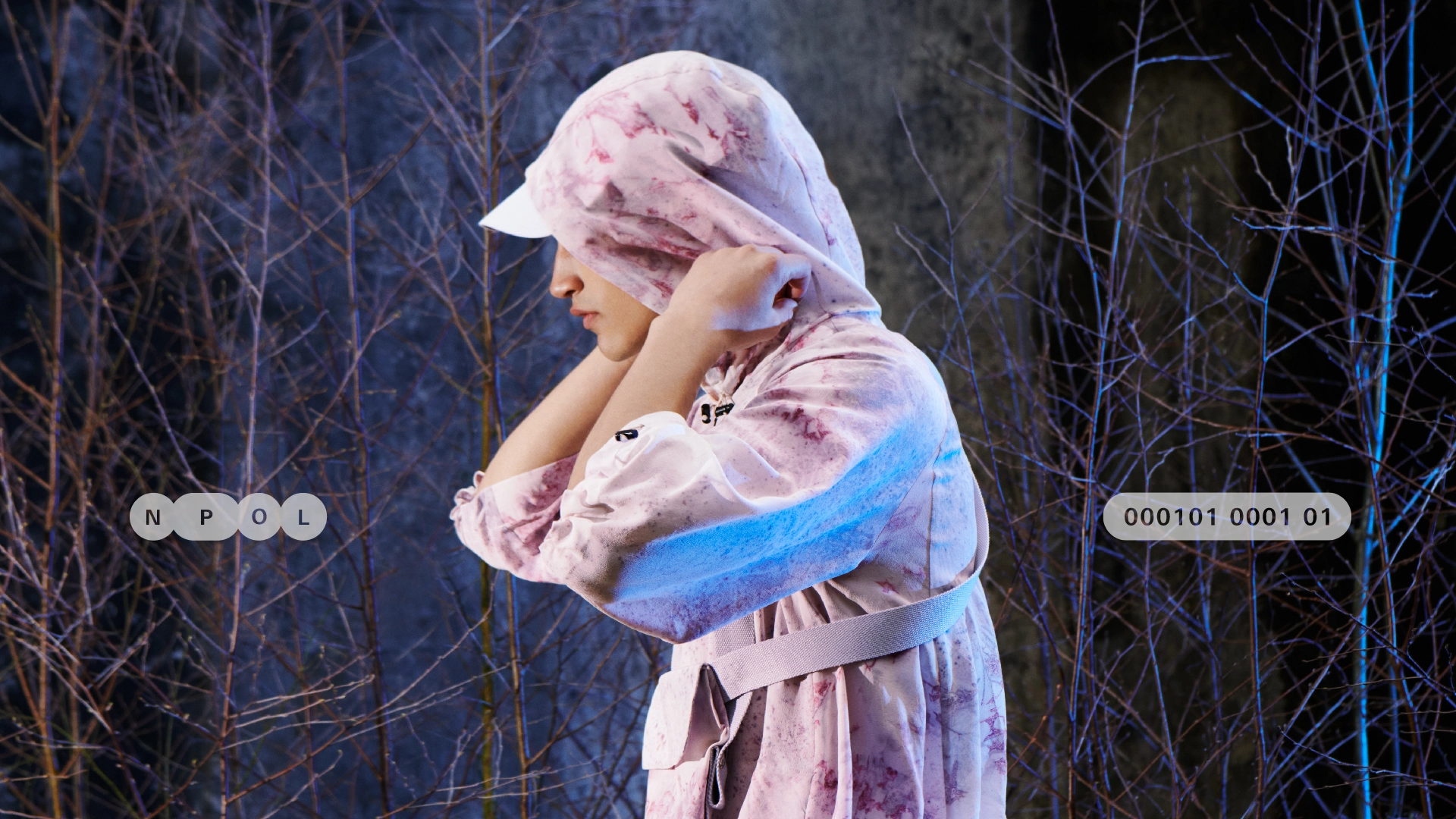 Profile of young man with trees in the background. He wears a microbial dyed silk technical hooded jacket.