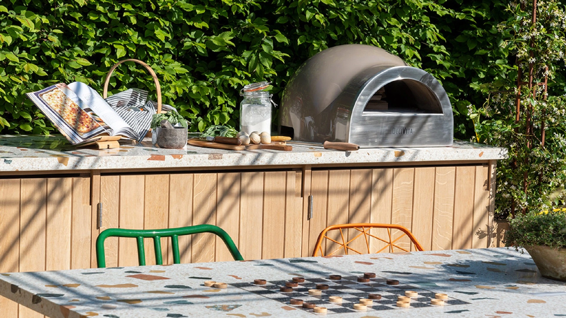 A photo of a table, two colourful chairs and a pizza oven in a garden