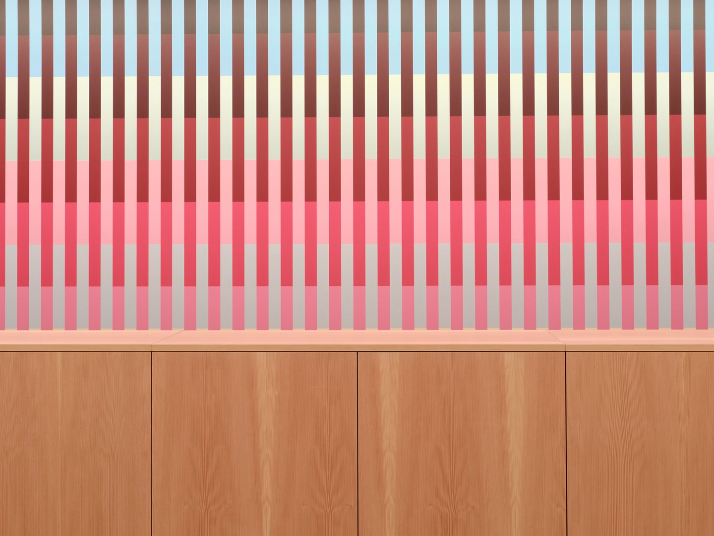 Maharam showroom wooden workstation in foreground and colorful gradient artwork with vertical rectangles in background.