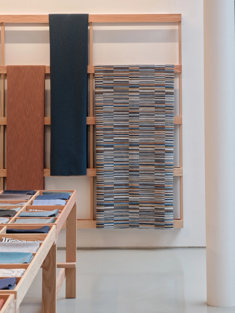Maharam showroom interior view of textiles hanging on a wall-mounted, wooden rack.
