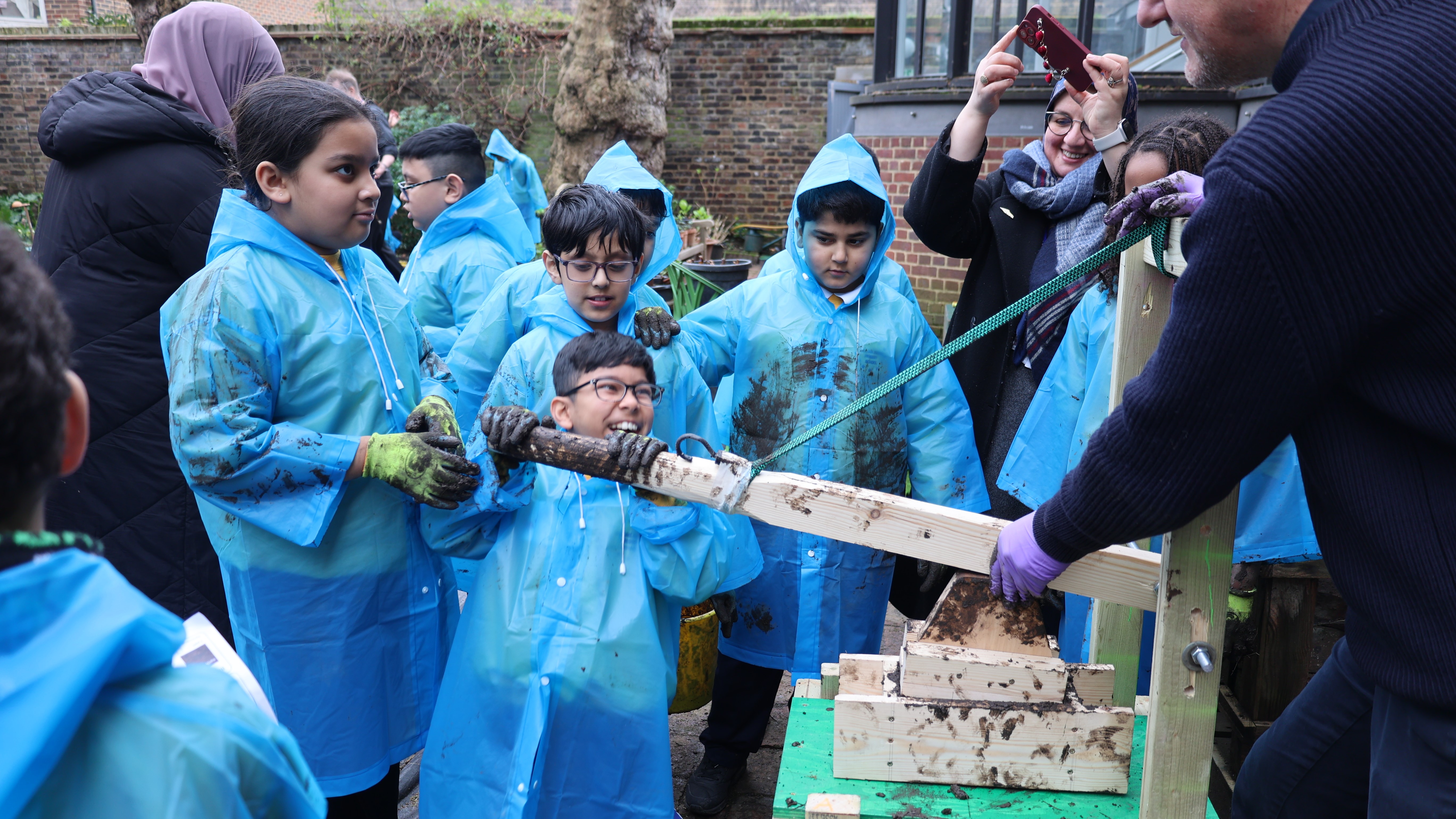 Primary school children in a garden workshop creating adobe bricks with a wooden machine