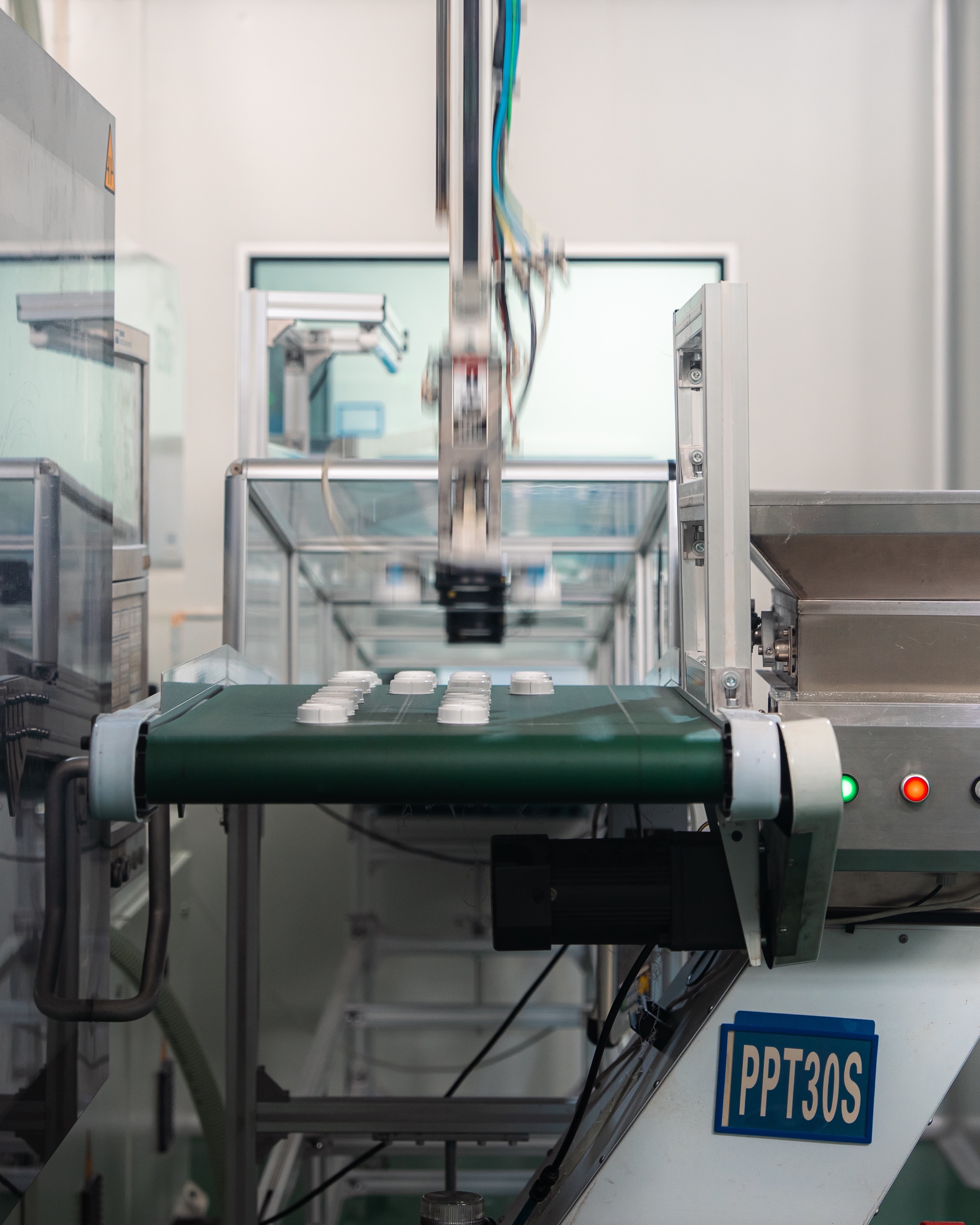 Industrial conveyor with robotic arm placing white plastic parts, inside a clean manufacturing line.