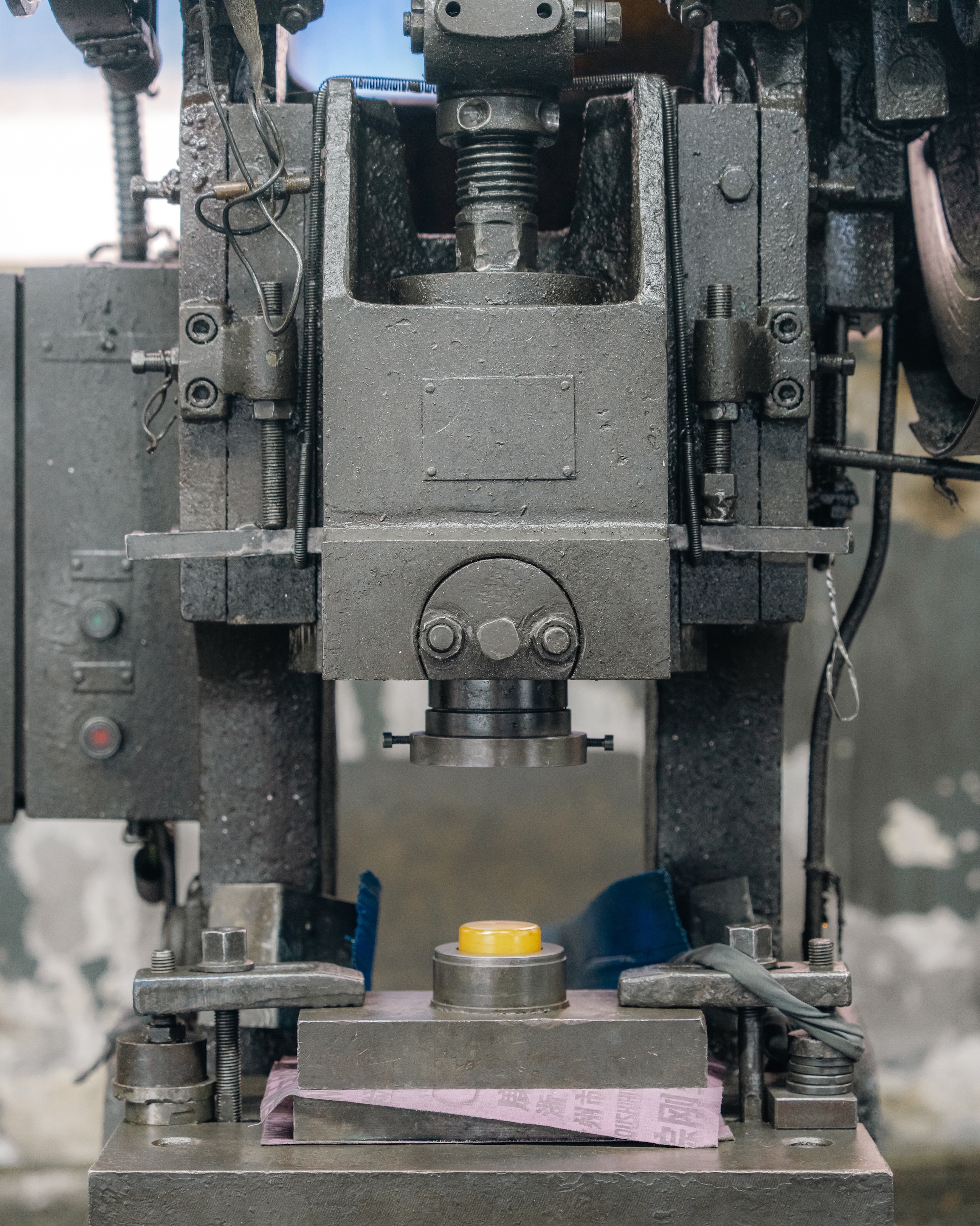 Close-up of an industrial metal stamping press, with die set and yellow component positioned on the worktable.