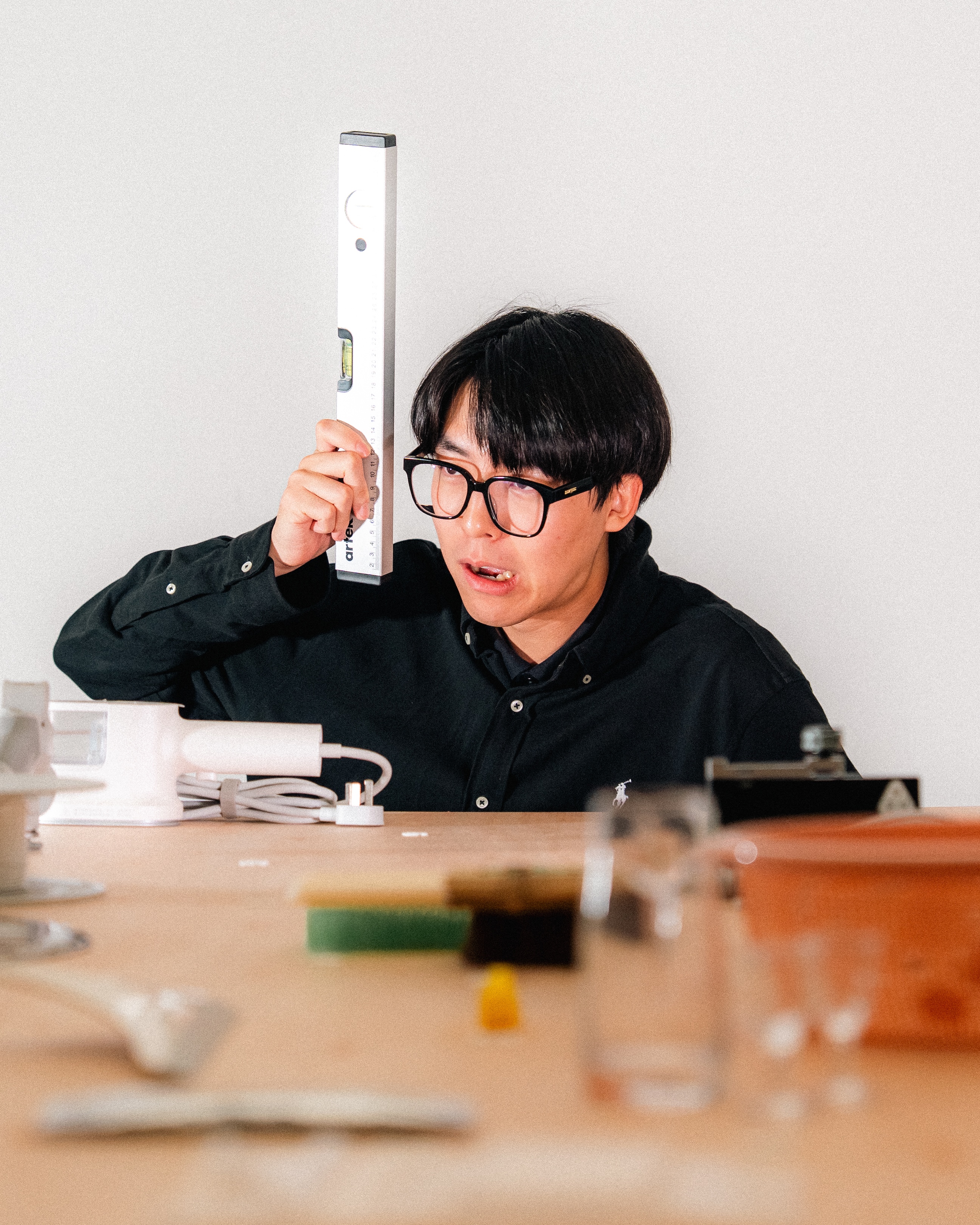 Person in black shirt and glasses holding a spirit level to their head.