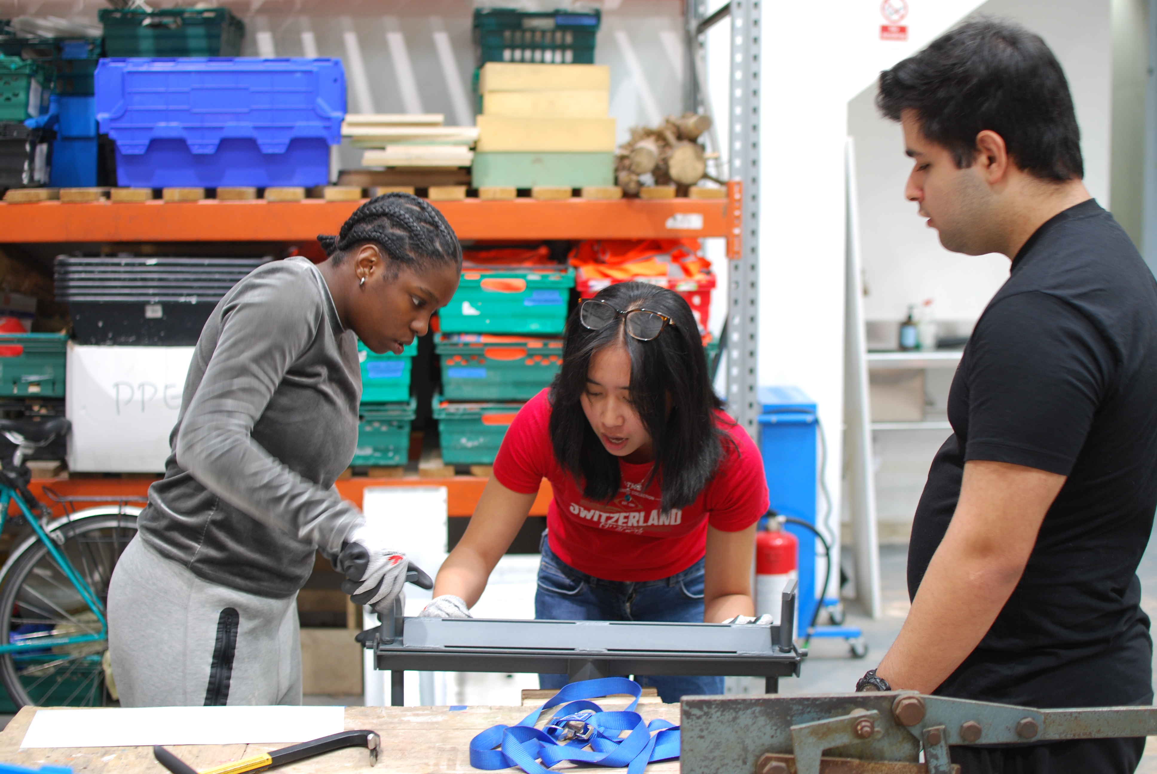 Three young people work with a grey metal folding machine, mounted on a bench, to fold the templates into the required shape.