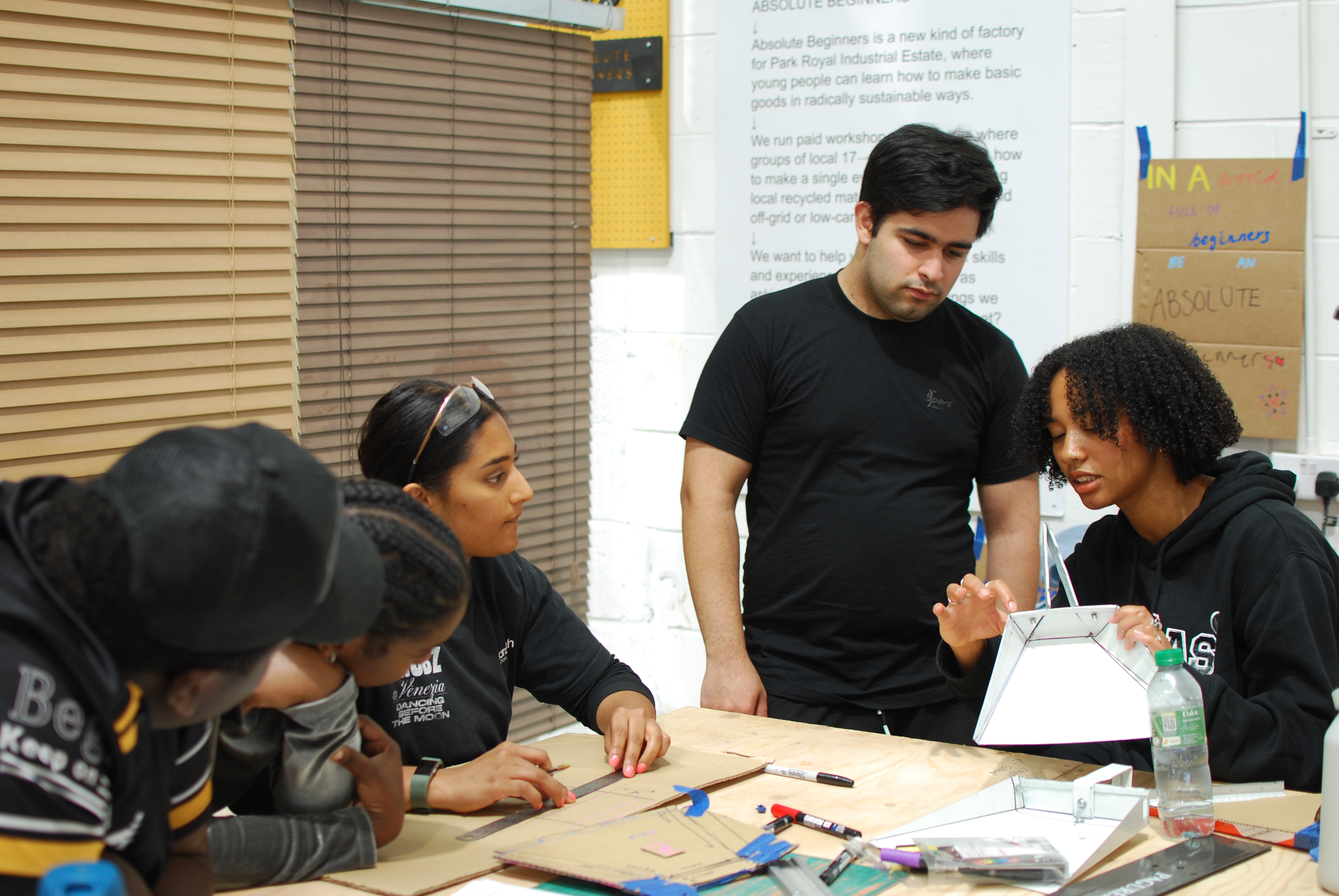 Five people sit around a workbench. One holds a prototype in her hands, whilst discussing it.