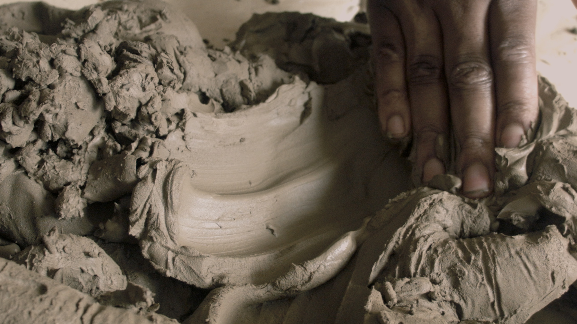 A hand pressing into brown clay leaving traces and marks