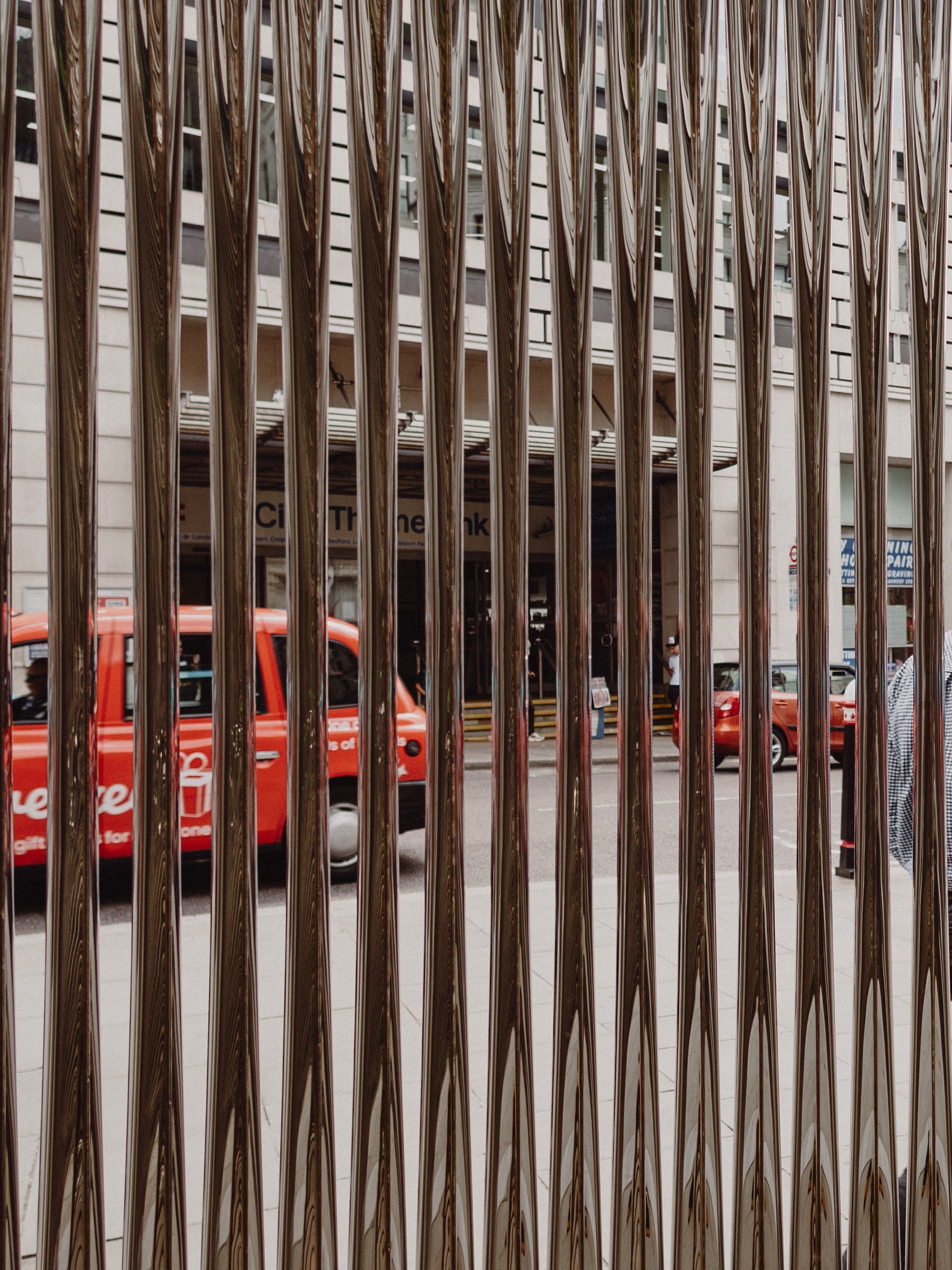 In the foreground, a shiny inflated-metal sculpture through which you can see a traditional London black cab