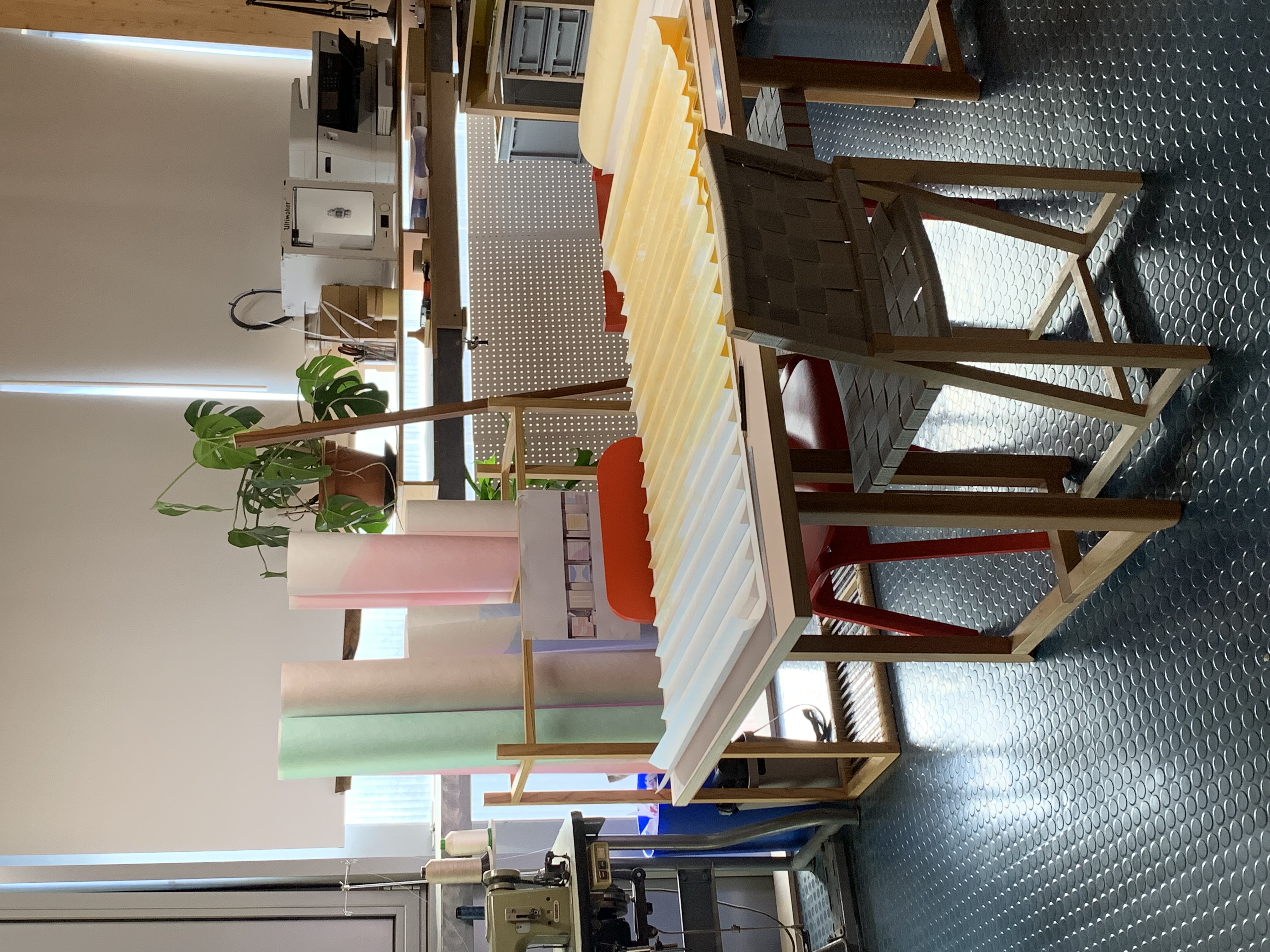 Yellow and white painted tyvek fabric folded into pleats on a table with chairs around it in a studio
