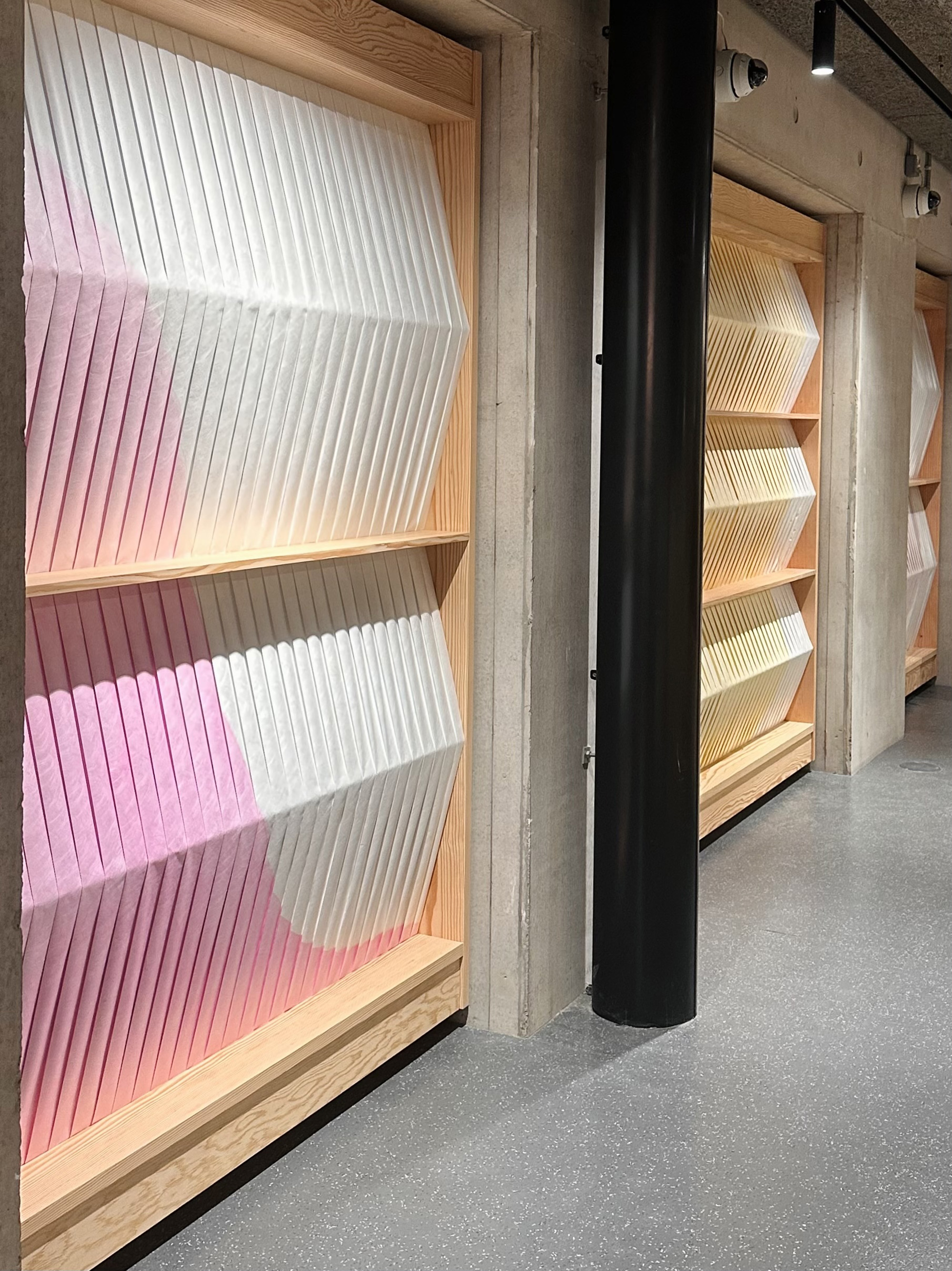 A series of colorful art work panels in pink, yellow and white along a concrete wall