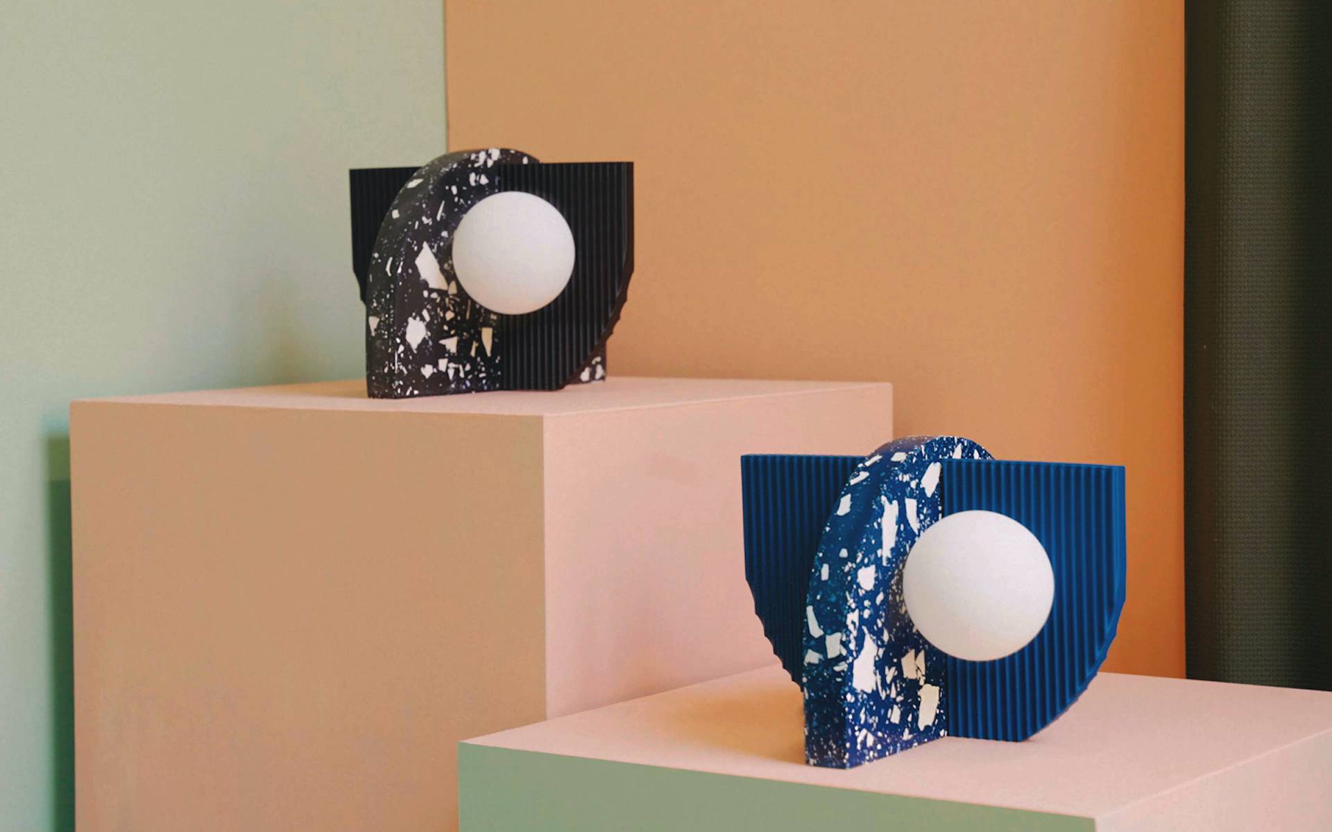 Two geometric table lamps, one black, one blue, sitting on pink plinths